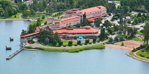 Un hotel grande de varios pisos con techo rojo, ubicado a la orilla de un lago con muelle y piscina.