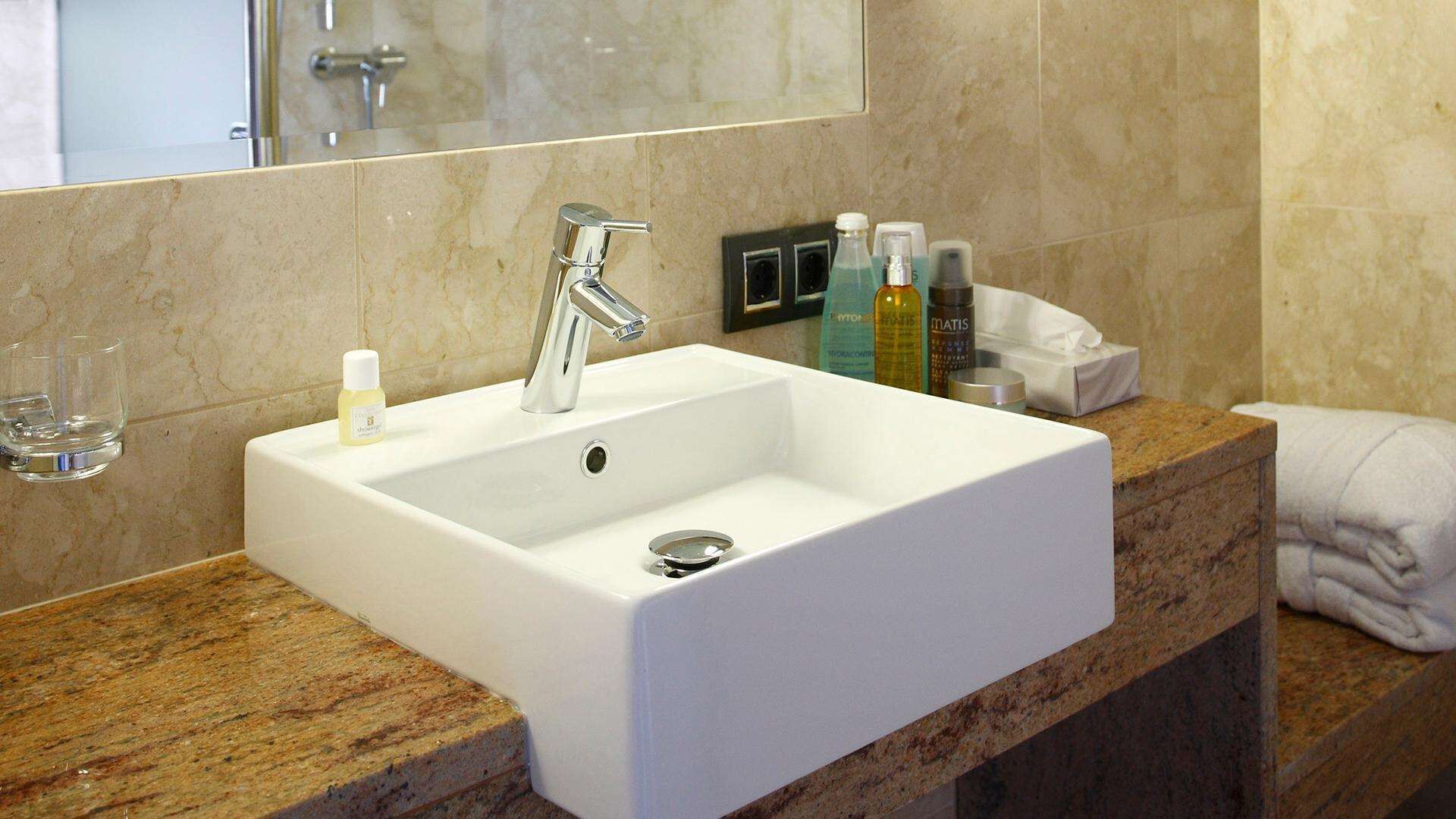 Ein Badezimmer mit einem weißen Waschbecken, einem Spiegel und Toilettenartikeln auf der Ablagefläche.