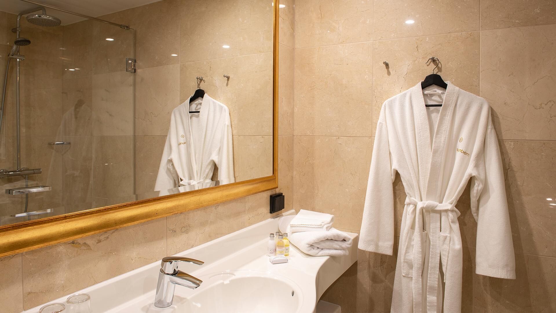 Ein Badezimmer mit einem großen Spiegel, einer Badewanne und zwei weißen Bademänteln, die an Haken hängen.