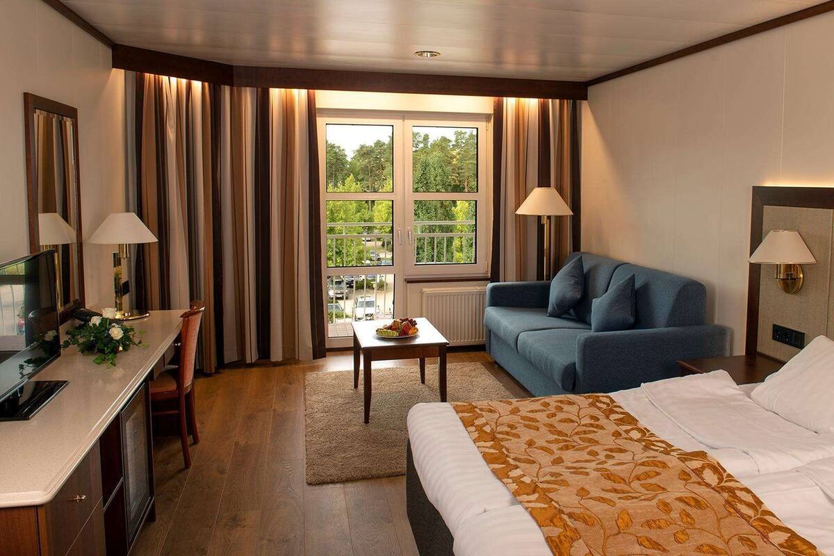 A hotel room with a bed, a desk, a chair, a sofa, and a window with curtains.