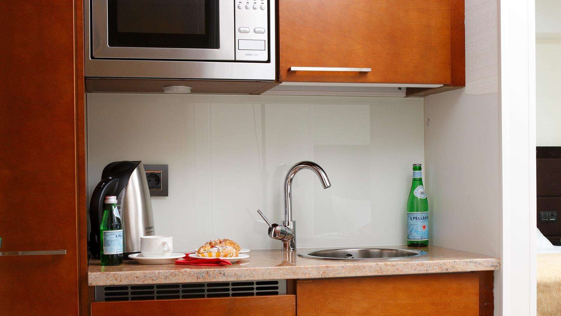 A compact kitchen with a microwave, coffee maker, and a bottle of S. Pellegrino water.