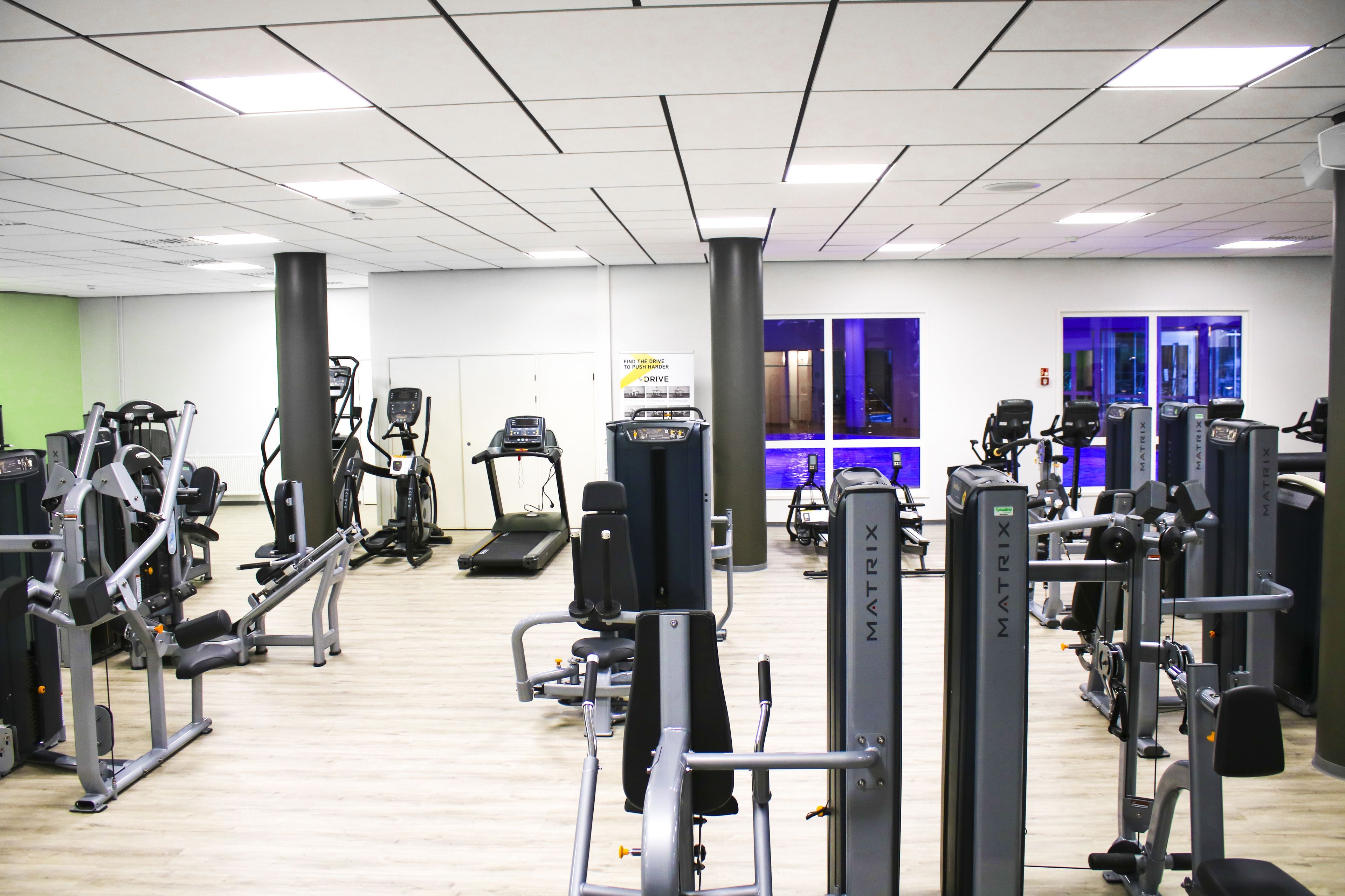 Un gimnasio con diversas máquinas de ejercicio, una cinta de correr y un pilar grande.
