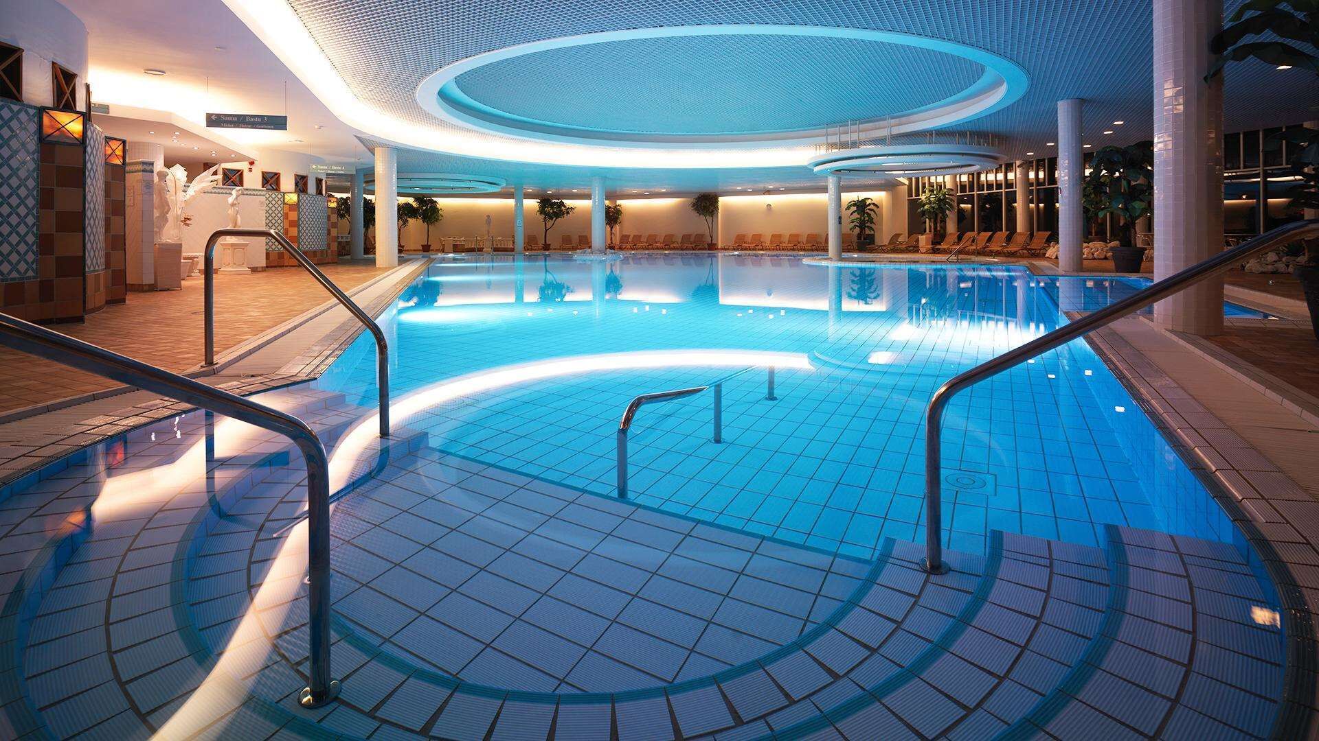 A large indoor swimming pool with a circular design, surrounded by lounge chairs and a modern ceiling structure.