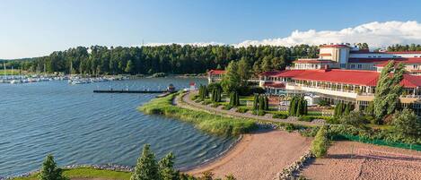 A lakeside hotel with a red-roofed building, a marina with boats, and a well-maintained beach area.