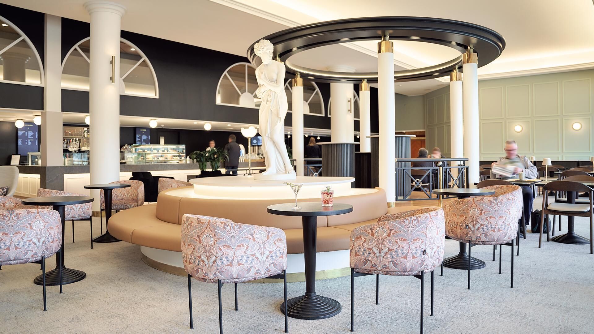 A modern lounge area with round tables, patterned chairs, and a central decorative column.