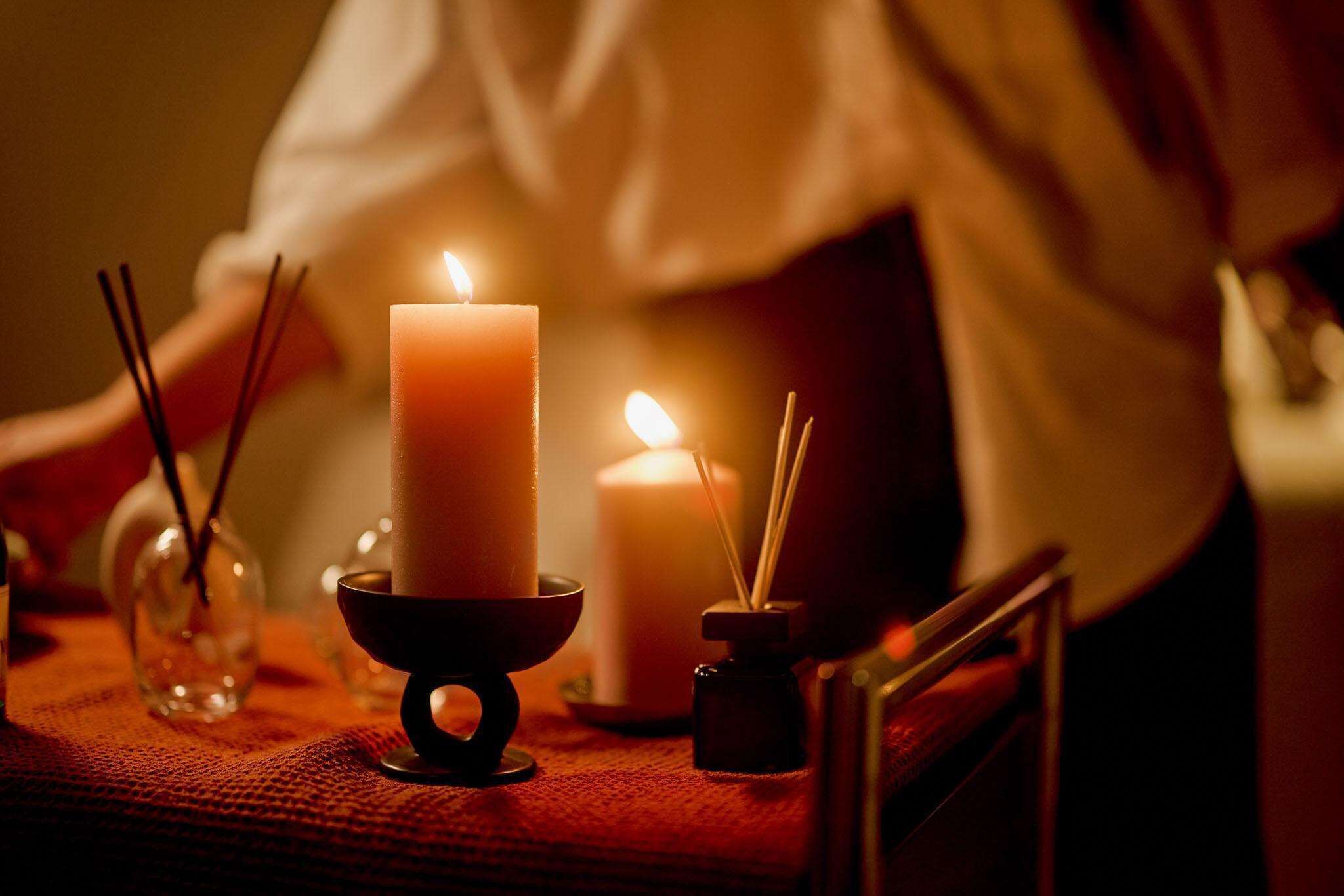 A candlelit table with a lit candle in a holder, a candle in a glass jar, and a small candle in a holder with a candle in a glass jar.