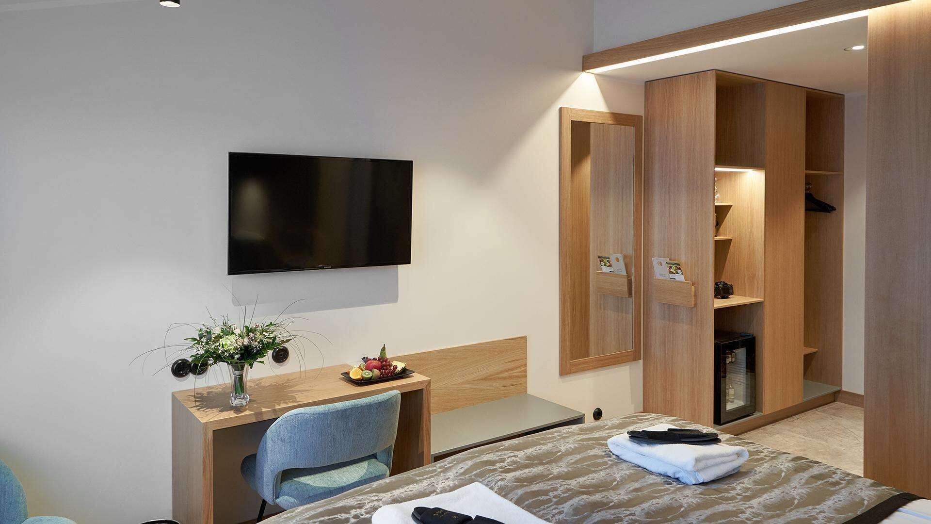 Une chambre d’hôtel comprenant un lit, un bureau avec une chaise, un téléviseur fixé au mur et une armoire avec un miroir.