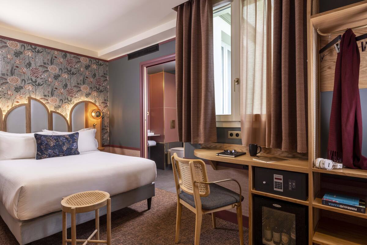Een hotelkamer met een bed, bureau, stoel, boekenkast en een minibar.