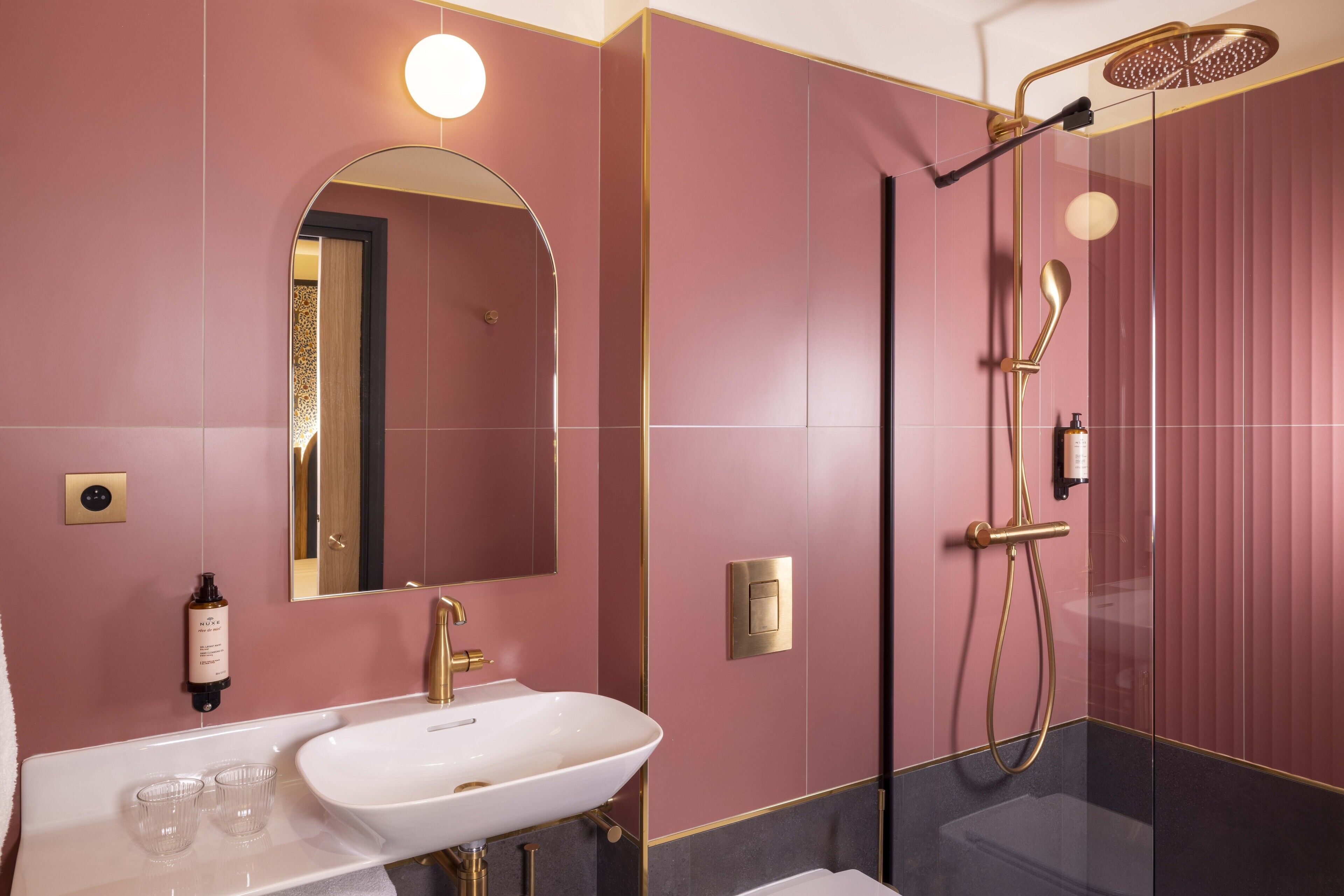 A modern bathroom with a white sink, a large mirror, and a gold showerhead.