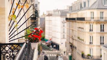 A narrow street with buildings on either side, a balcony with a flower pot, and a clear view of the street below.