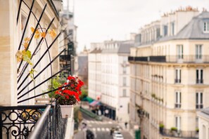 A narrow street with buildings on either side, a balcony with a flower pot, and a clear view of the street below.