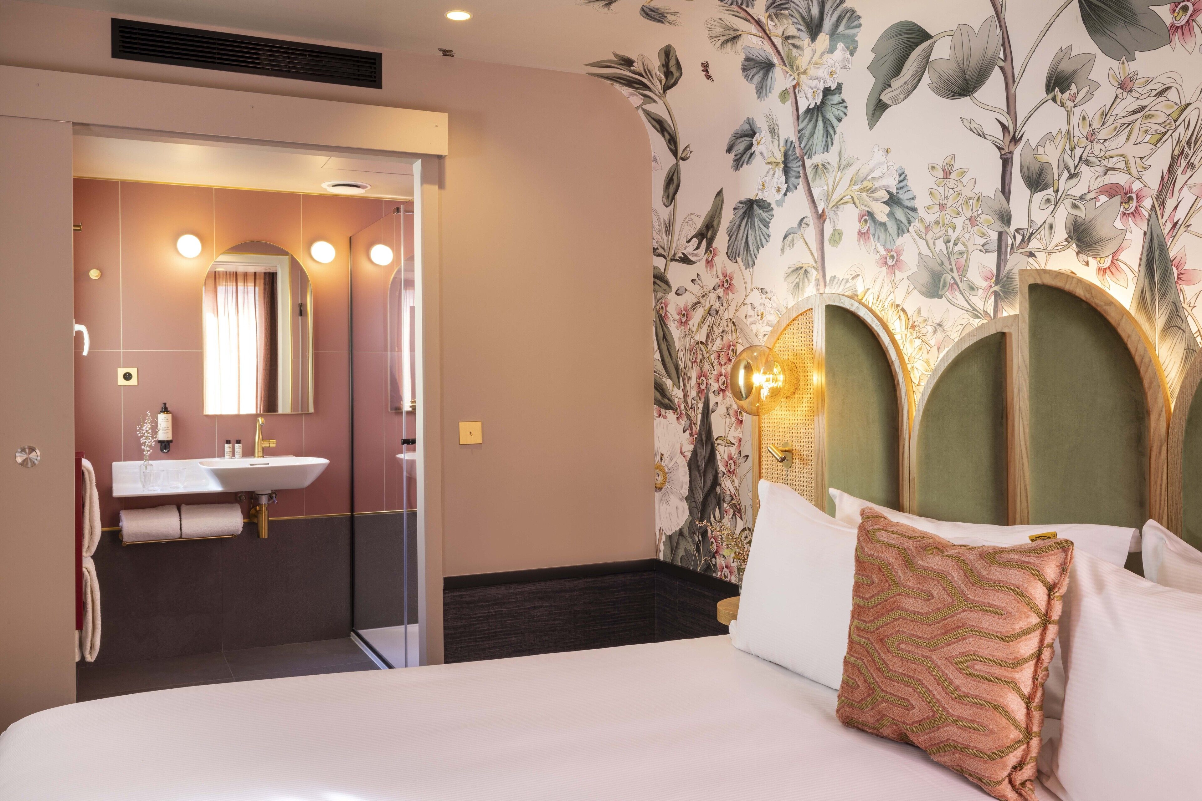 A hotel room with a bed, a bathroom with a sink and mirror, and floral wallpaper.