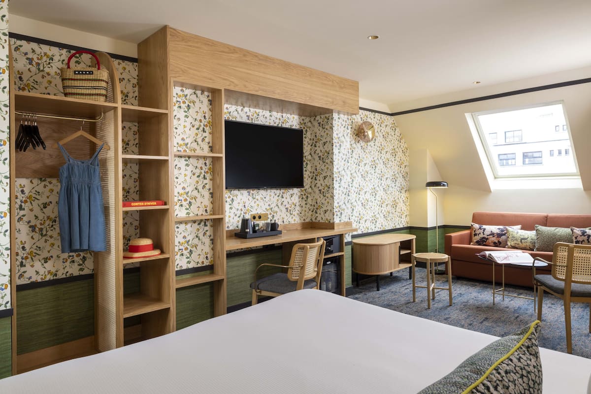 Hotelkamer met een bed, een bureau met stoel, een bank, een televisie en een raam met uitzicht op gebouwen.