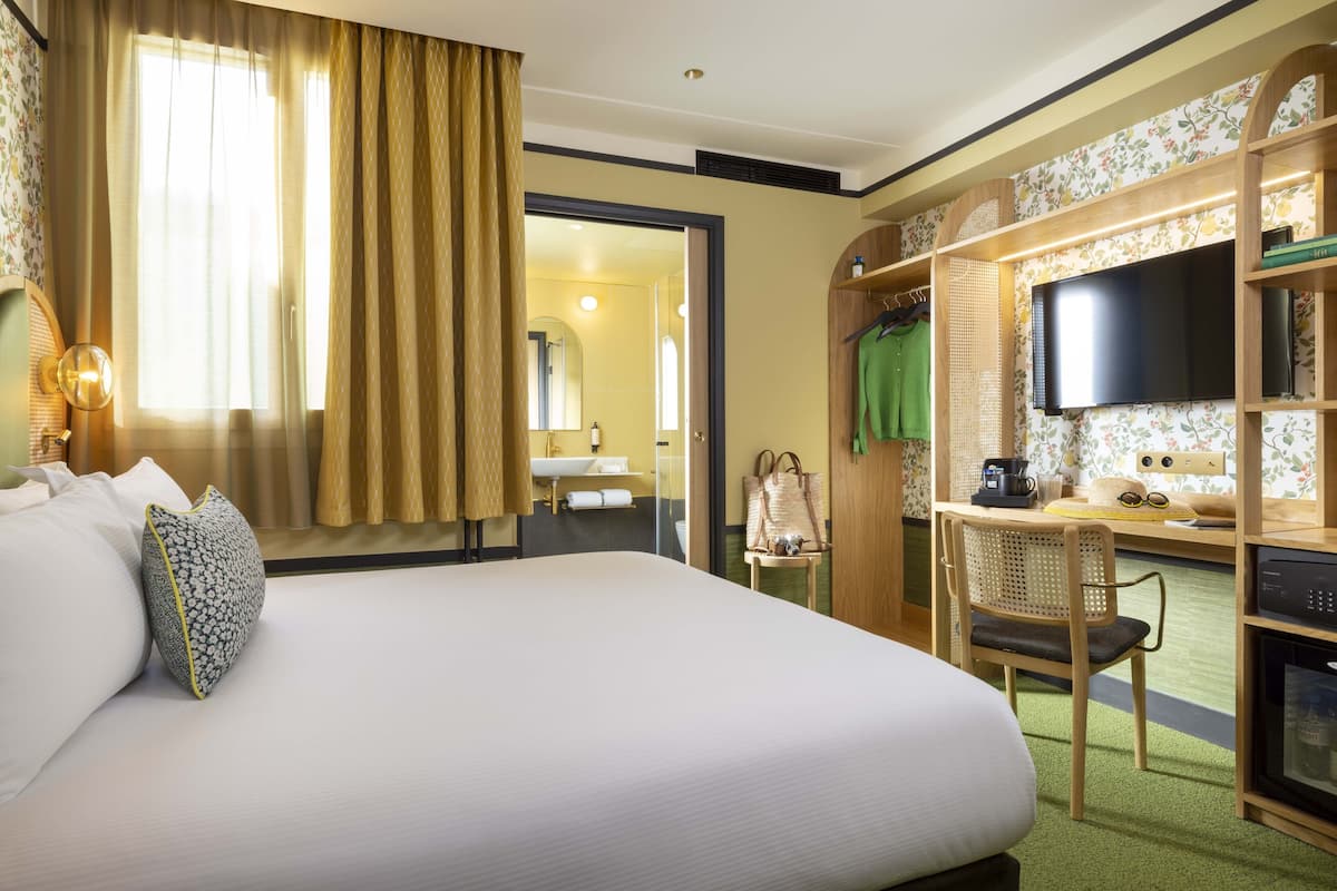 Een hotelkamer met een groot bed, een bureau met stoel, een televisie en een kledingkast.