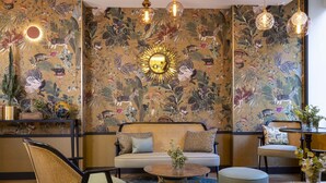 Une pièce comprenant un canapé, des fauteuils, une table basse ronde et un mur décoré d’un motif.