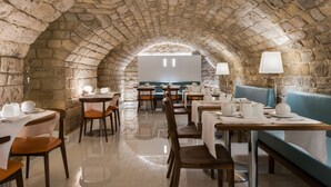 Un restaurant doté d’un plafond en pierre en forme d’arc, avec des tables, des chaises et un coin salon bleu.