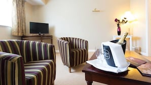 A living room with striped armchairs, a flat-screen TV, a table with a champagne bottle and glasses, and a vase with flowers. - Roman Way Hotel A5 Cannock (Cannock)