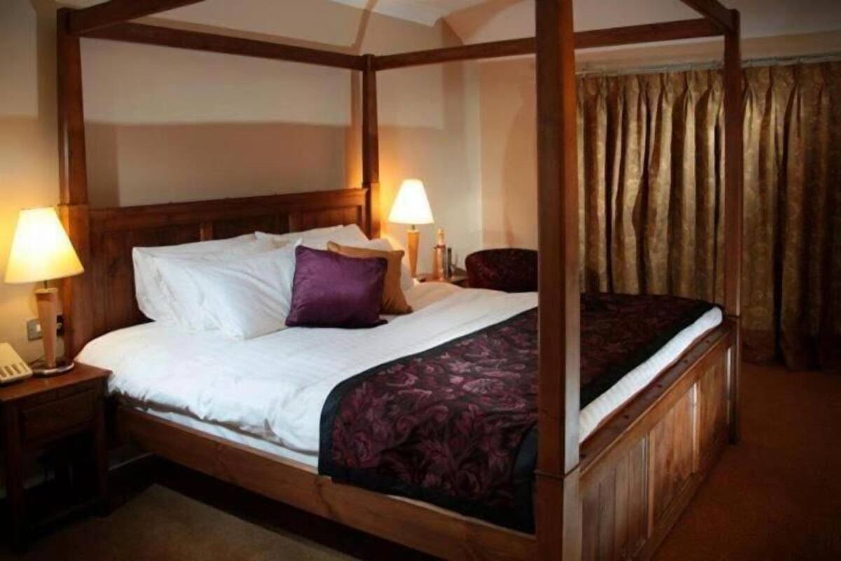 A four-poster bed with white linens and a purple throw pillow, flanked by two bedside tables with lamps.
