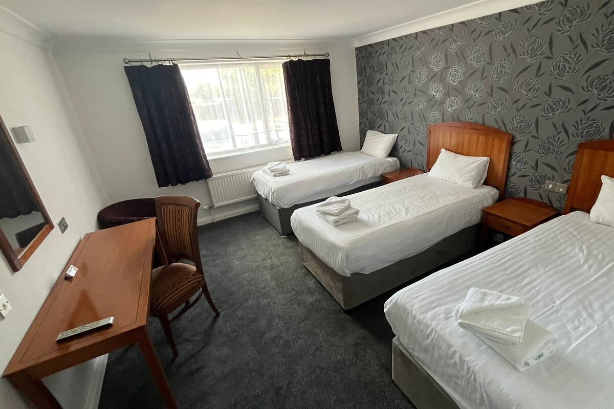 A hotel room with two single beds, a desk, a chair, and a window with curtains.