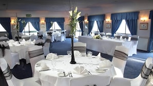 A banquet hall with round tables set for a formal event, featuring white tablecloths, black chair sashes, and floral centerpieces. - Roman Way Hotel A5 Cannock (Cannock)