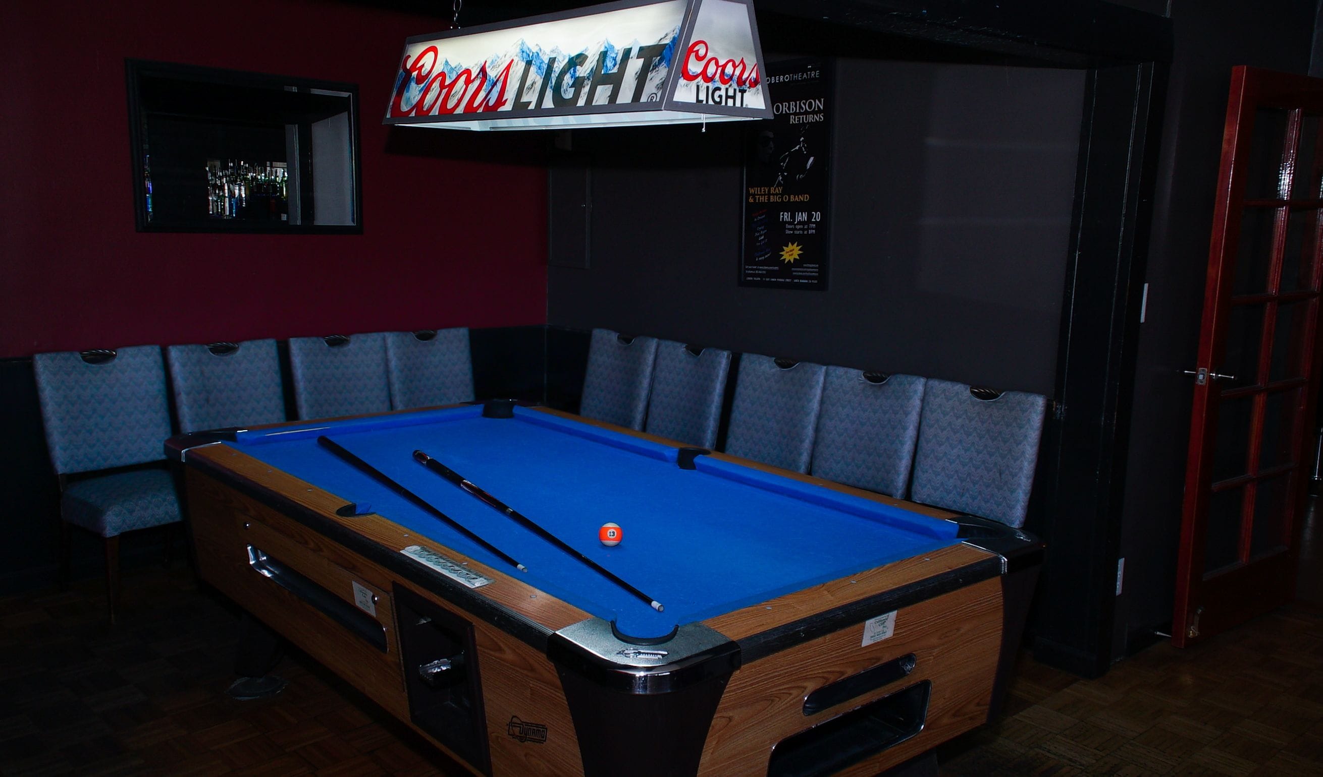 A pool table in a room with a Coors Light sign above.