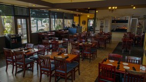 A restaurant with wooden tables and chairs, a bar area, and large windows with a view of the outdoors. - San Simeon Lodge (San Simeon)