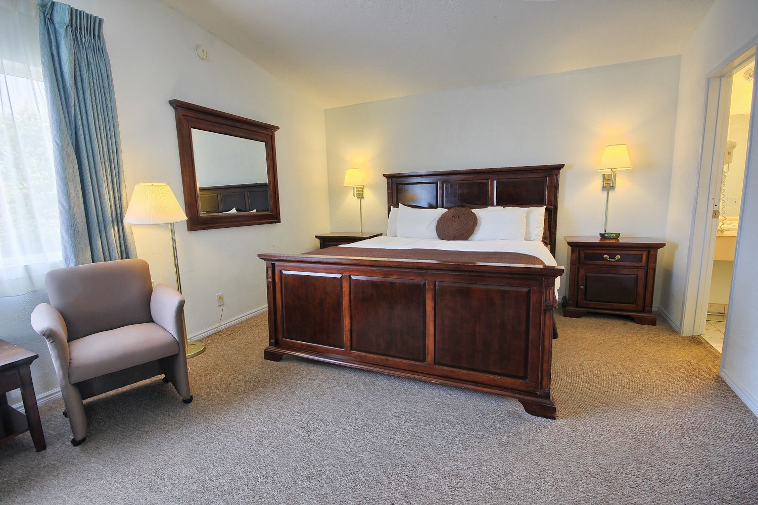Une chambre d’hôtel avec un grand lit, deux tables de chevet avec des lampes, une chaise et un miroir au mur.