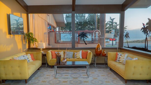 A modern living room with yellow sofas, a glass coffee table, and a large window offering a view of the beach and palm trees. - San Simeon Lodge (San Simeon)