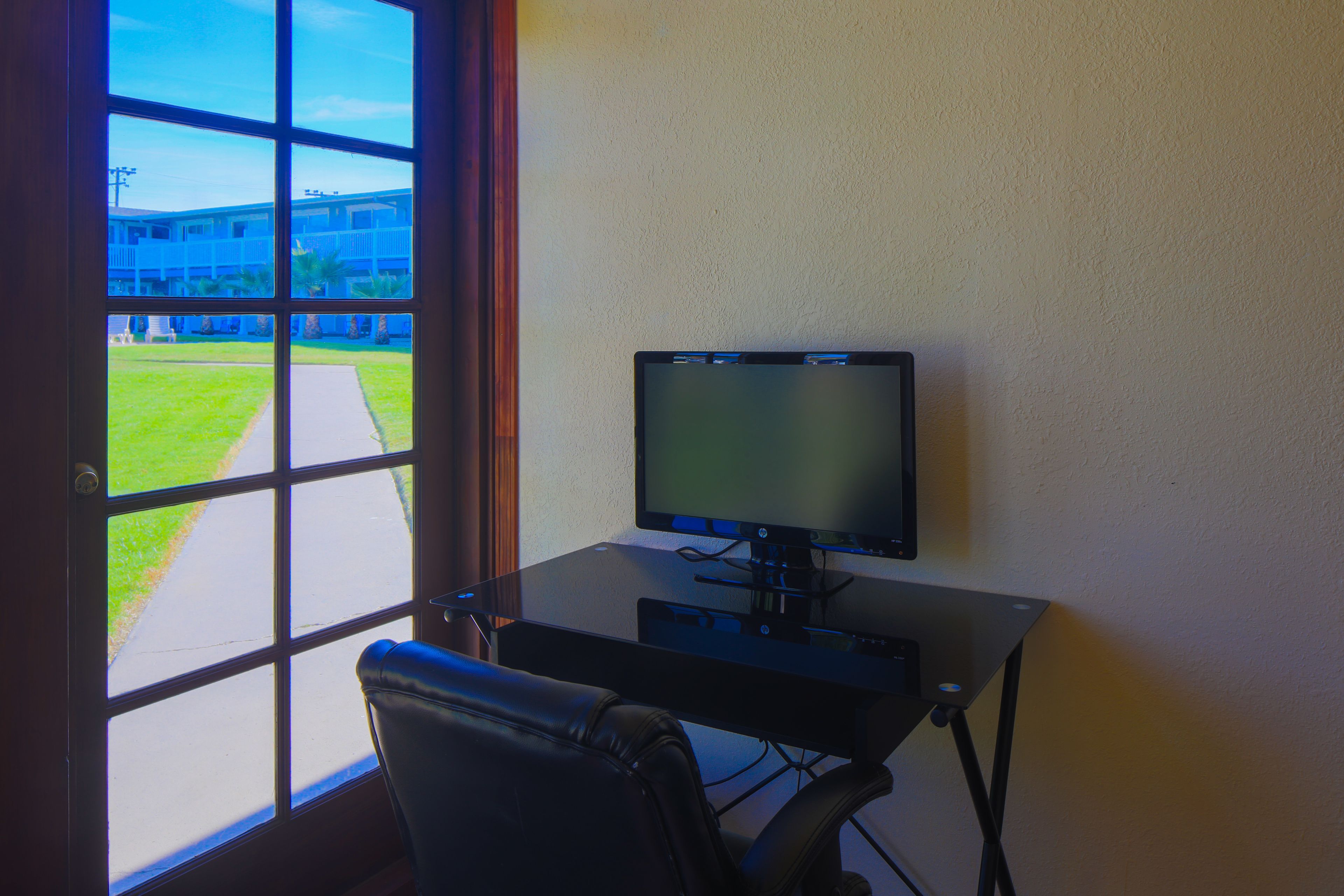 A room with a desk, a computer, and a window overlooking a building and a pathway.