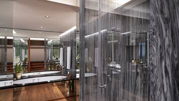 A modern bathroom with a large mirror, marble walls, and a wooden floor.