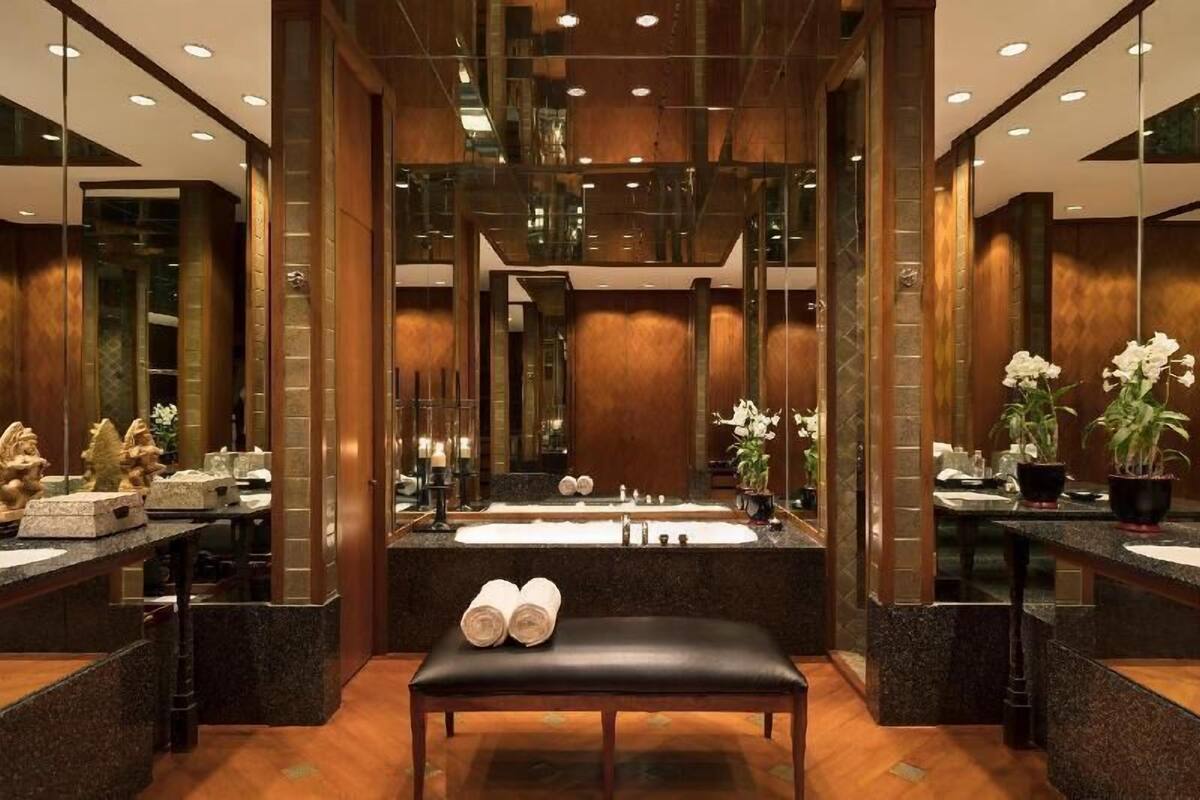 A modern bathroom with a large mirror, a bench, and two sinks.