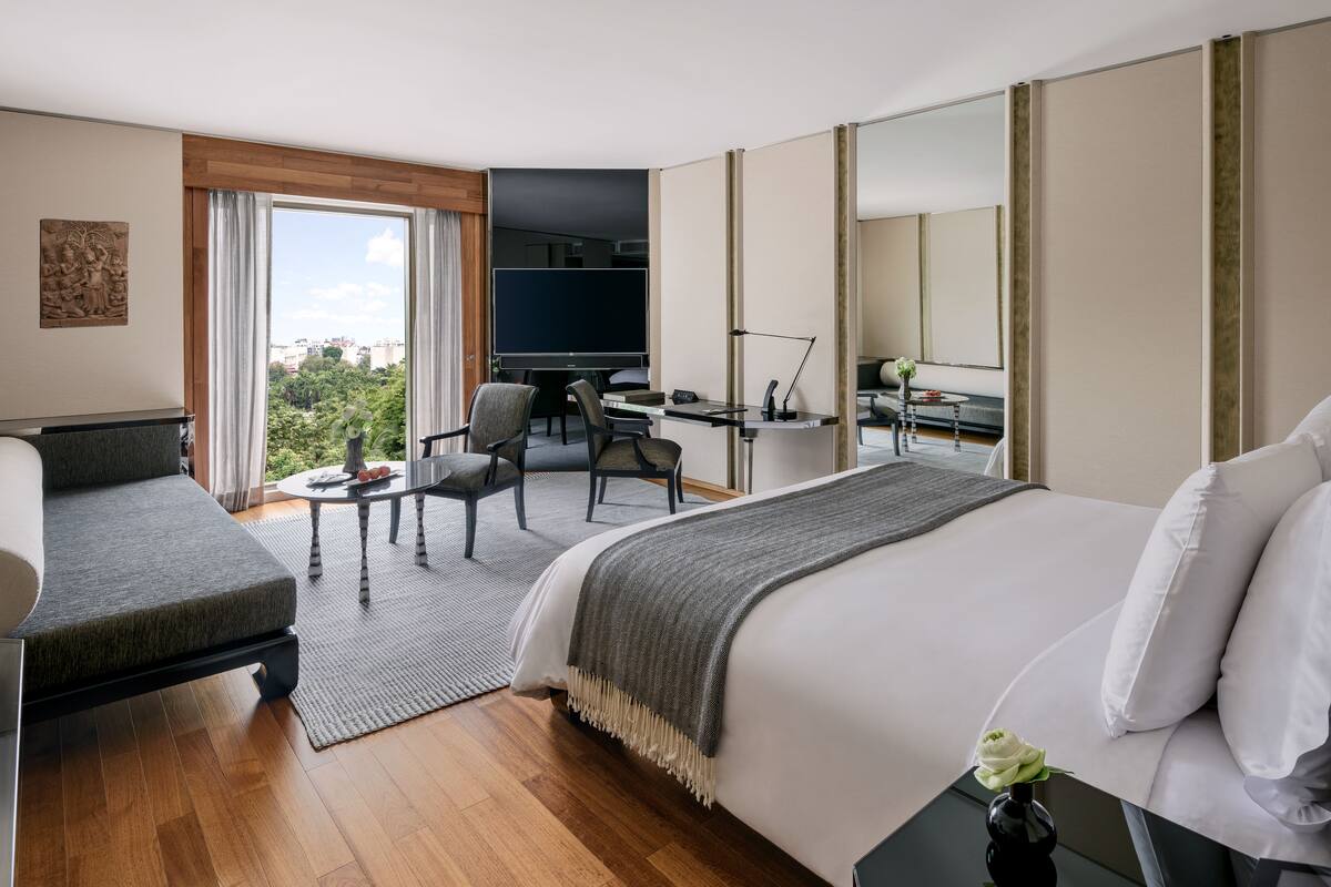 A modern hotel room with a large bed, a desk, a chair, and a view of the outdoors.