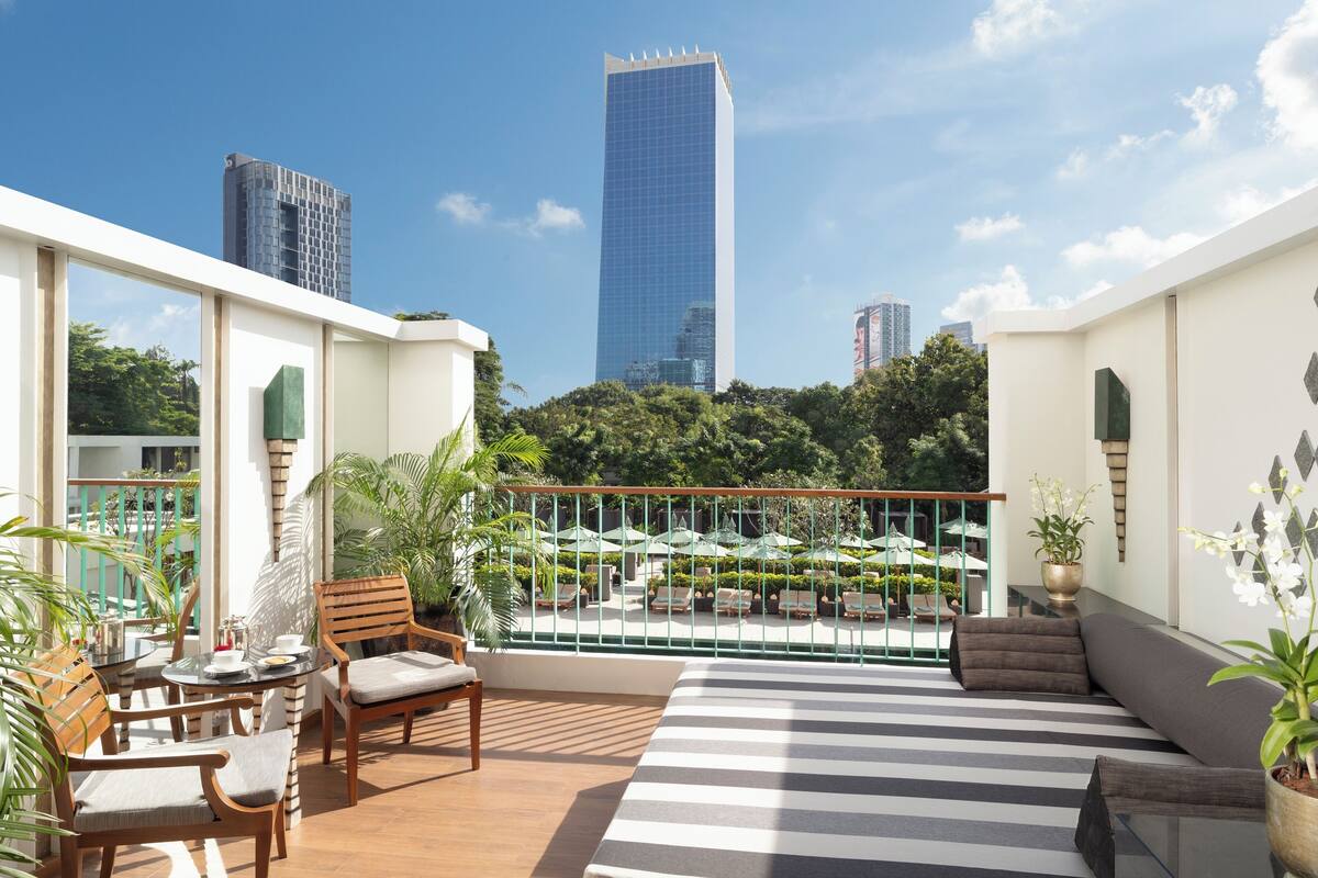 A modern balcony with a view of a tall skyscraper, wooden furniture, and potted plants.