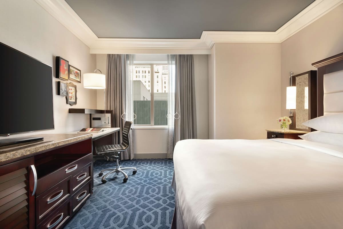 A hotel room with a large bed, a desk with a chair, a television, and a window with curtains.