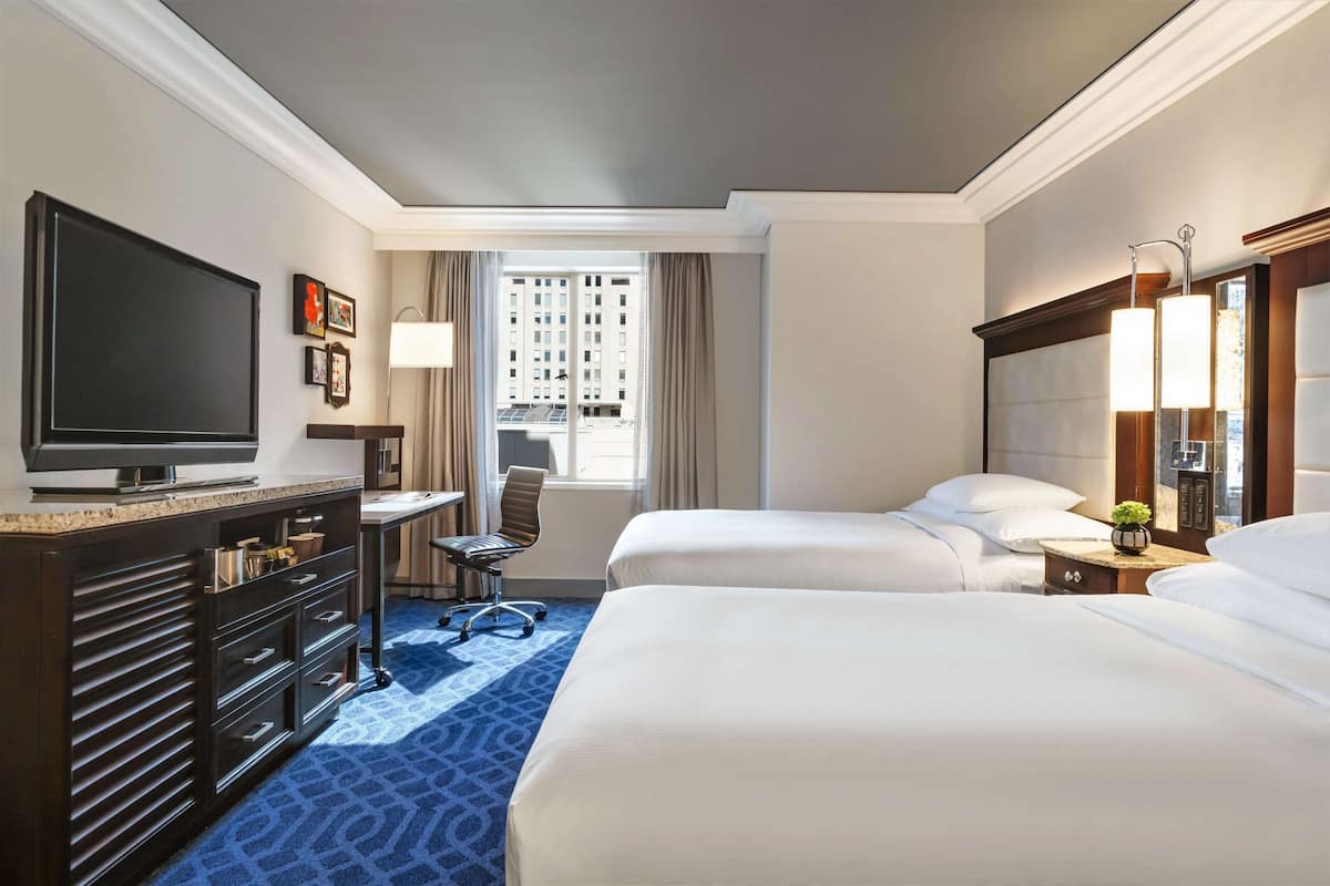 A hotel room with two beds, a desk with a chair, a television, and a window with curtains.