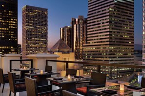 A rooftop dining area with tables and chairs, overlooking a cityscape with tall buildings. - Hilton Checkers Los Angeles (Los Angeles)