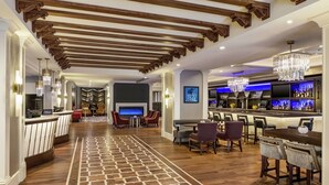 En hotellobby med træloft, et mønstret tæppe, en receptionsdisk, et barområde og siddepladser.