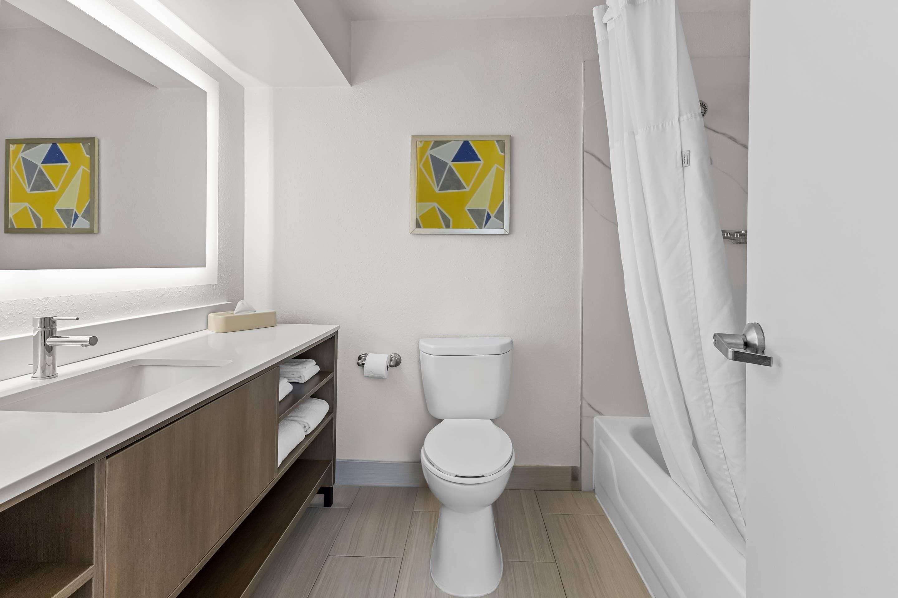 Un baño moderno con lavamanos, inodoro y ducha blancos. Hay dos obras de arte enmarcadas en la pared.