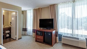 A hotel room with a bed, a TV, a microwave, a mini-fridge, a vanity with a mirror, and a large window with curtains. - Comfort Inn Elizabeth City near University (Elizabeth City)