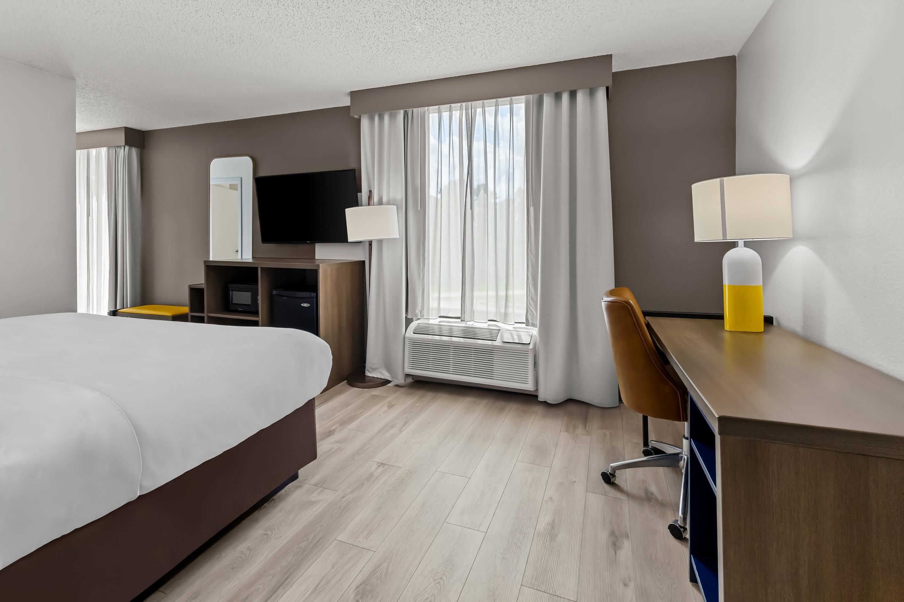 A hotel room with a bed, a desk, a chair, a TV, and a window with curtains.
