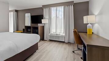 A hotel room with a bed, a desk, a chair, a TV, and a window with curtains.
