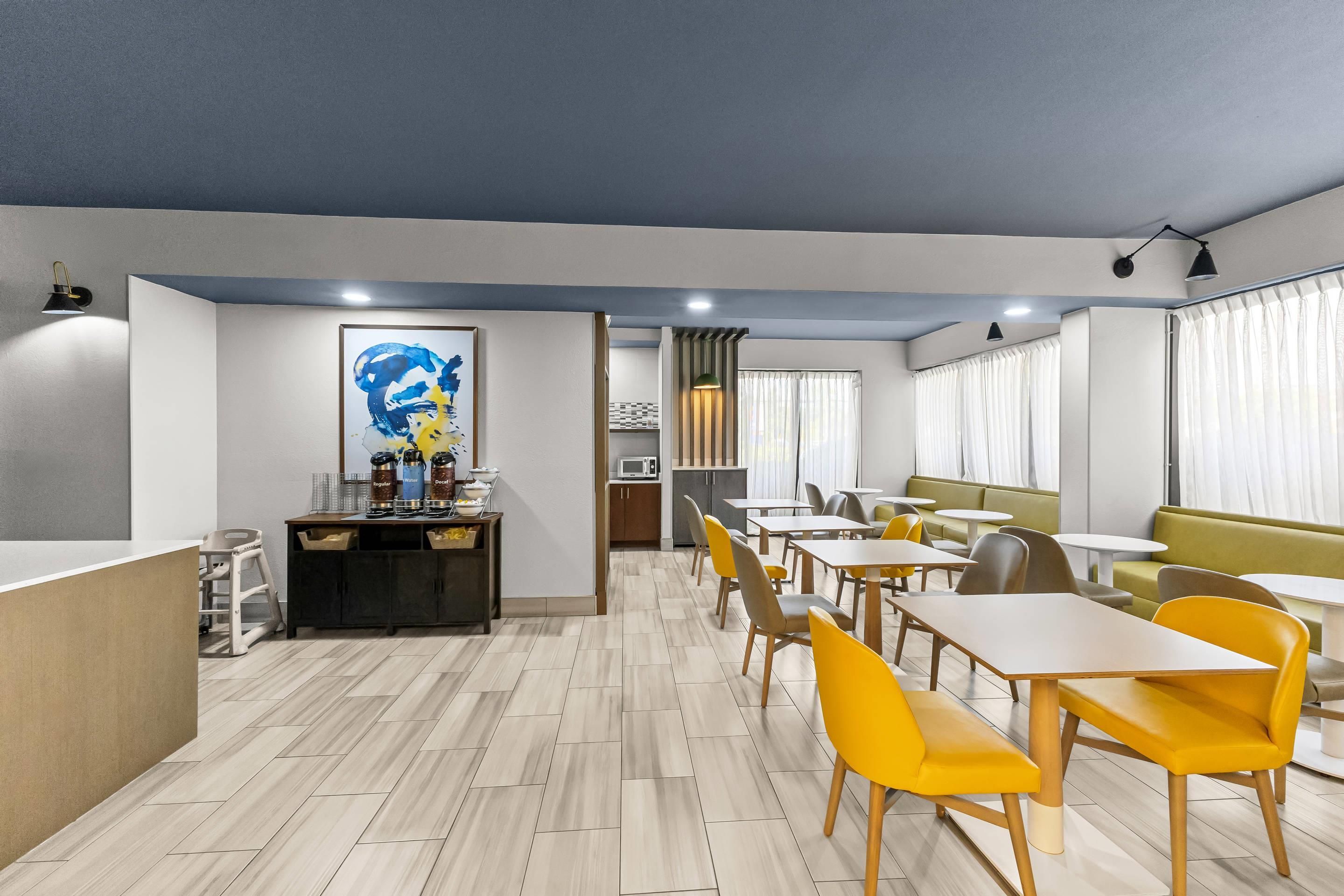 A modern dining area with wooden flooring, yellow chairs, and a central counter with a coffee machine.