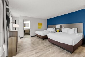 Una habitación de hotel con dos camas, baño y vista al pasillo.