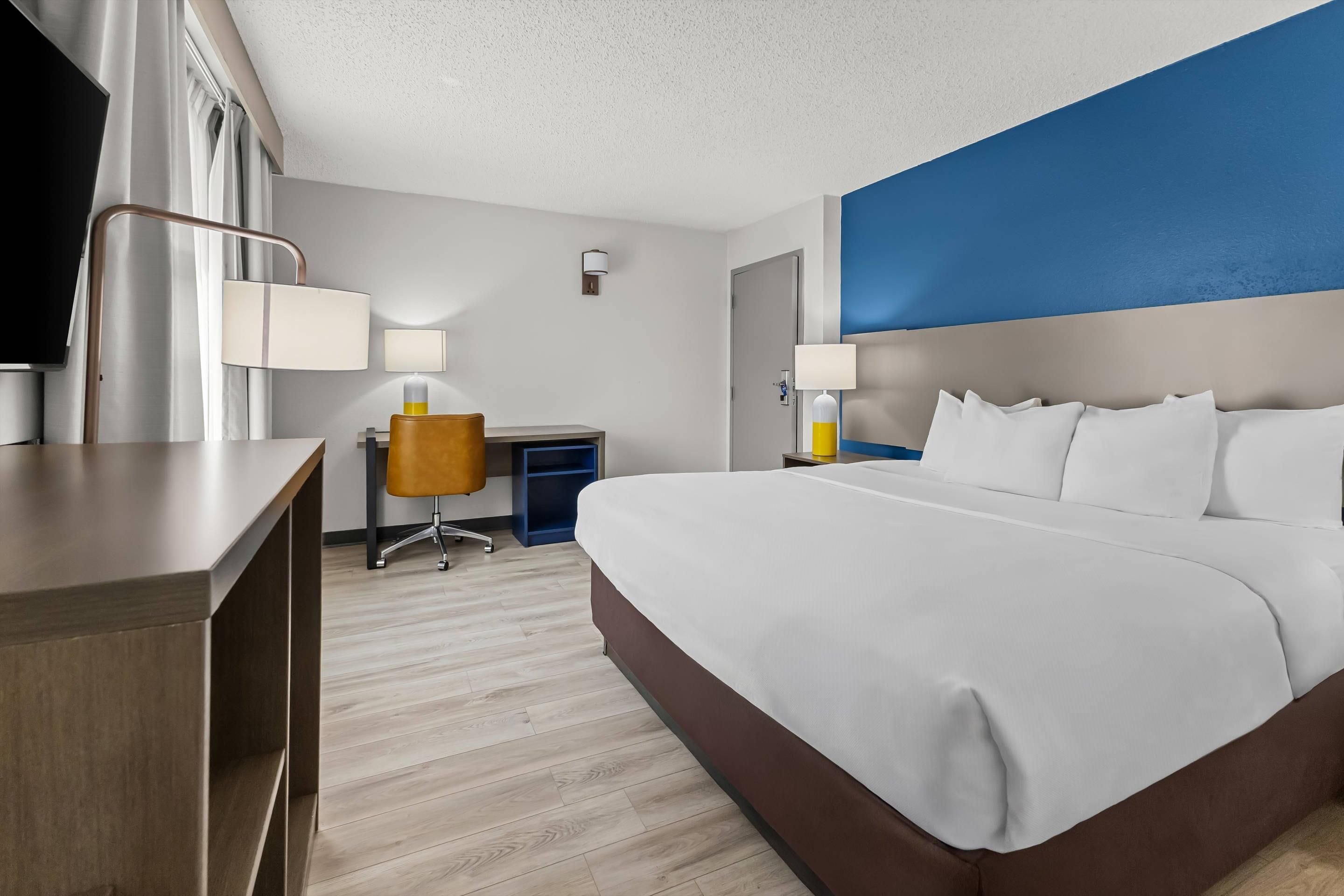 A hotel room with a large bed, a desk, a chair, and a television.