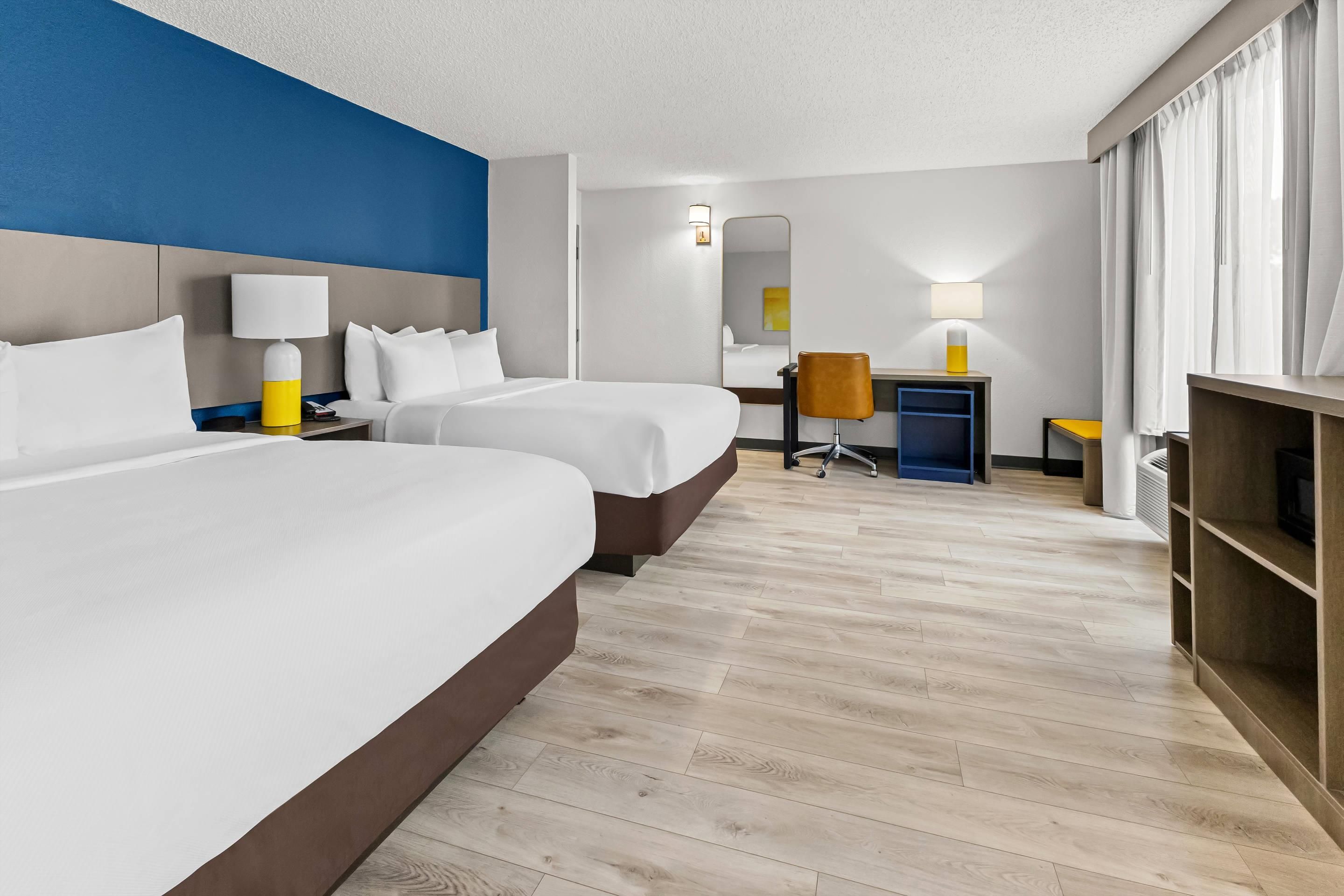 Une chambre d’hôtel avec deux lits, un bureau, une chaise et une armoire.