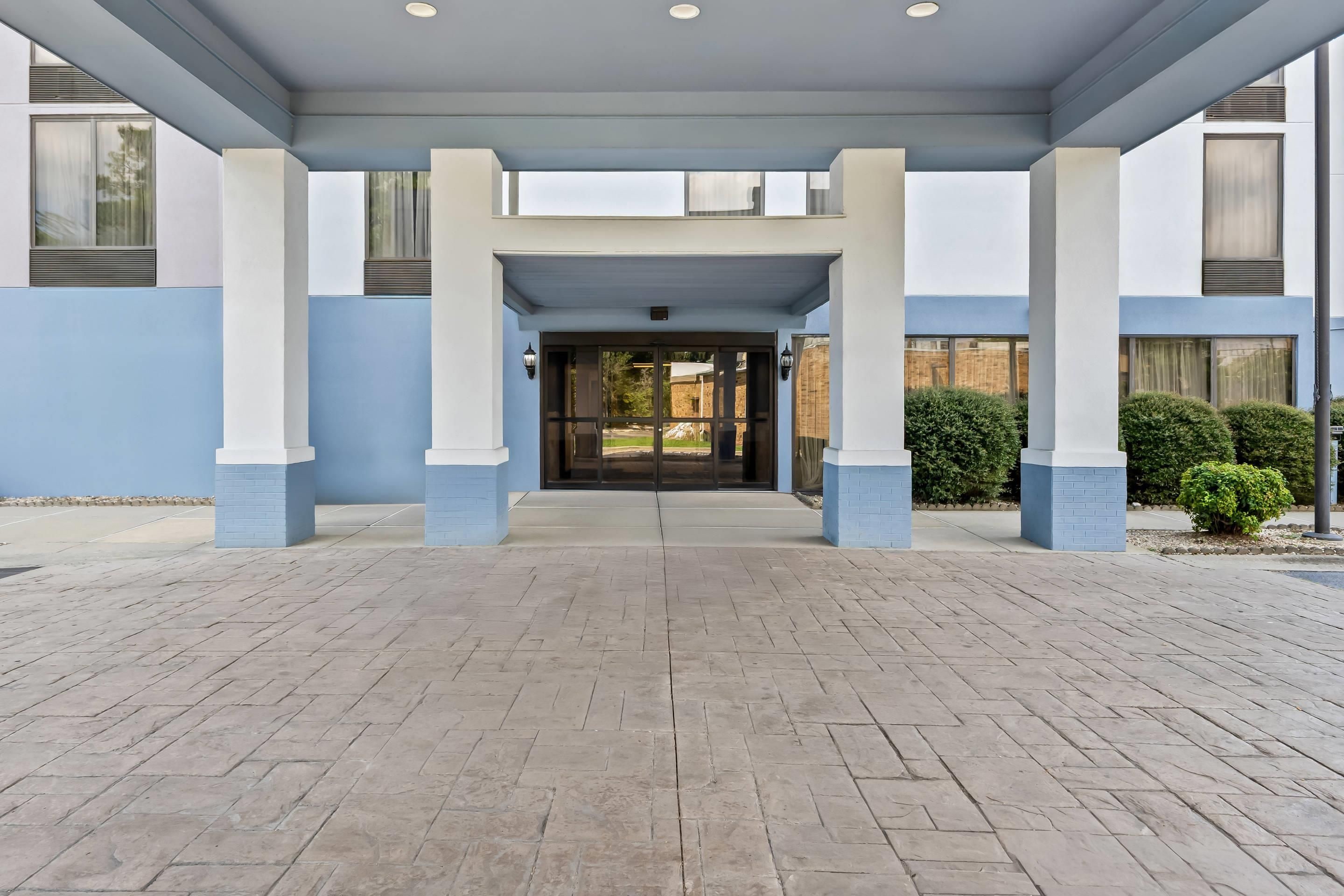 A covered entrance with a brick floor leading to a building with large windows and a blue and white color scheme.