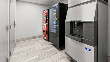 A vending machine and a water dispenser in a hallway with a tiled floor.