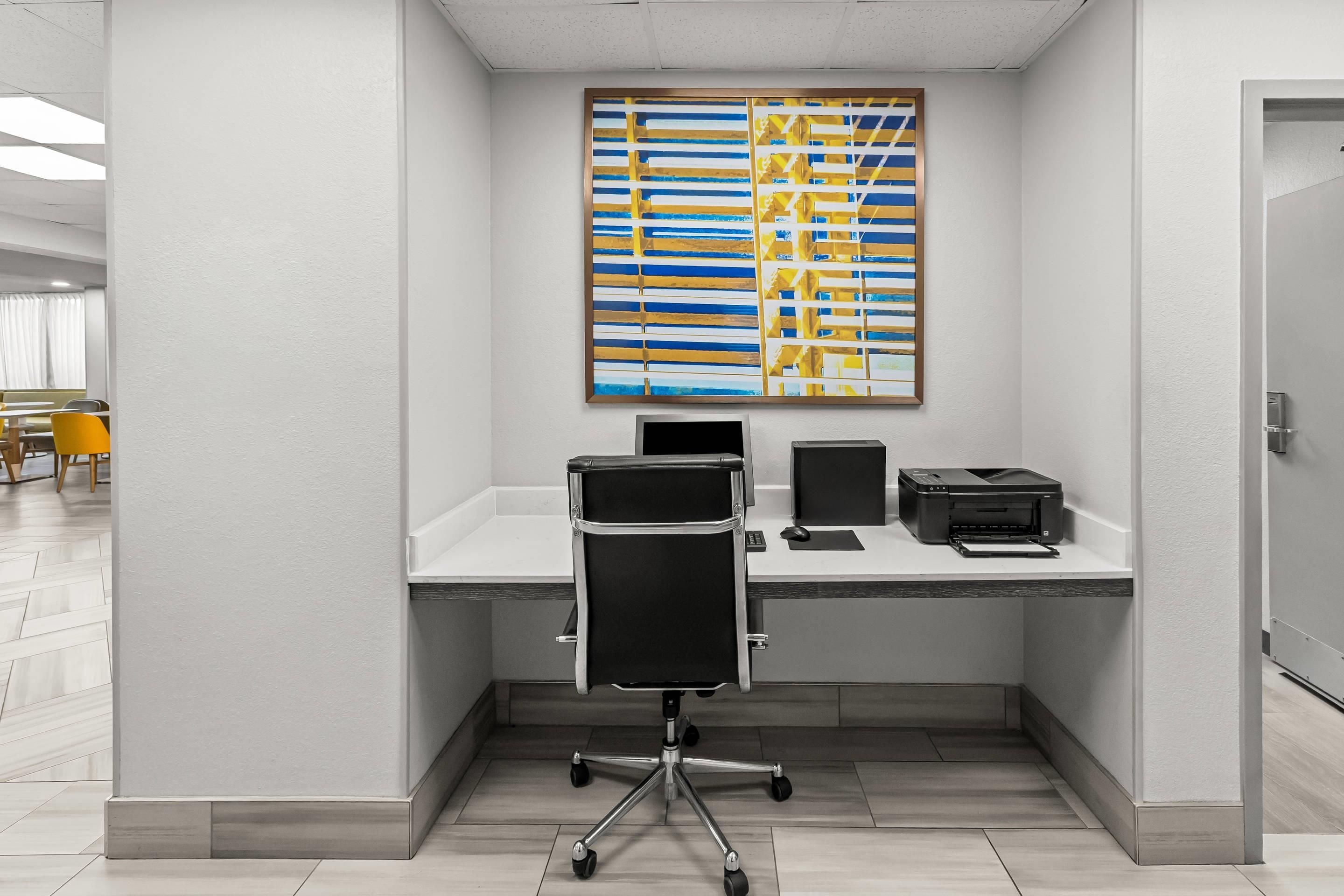 A modern office space with a desk, two chairs, a printer, and a large abstract painting on the wall.