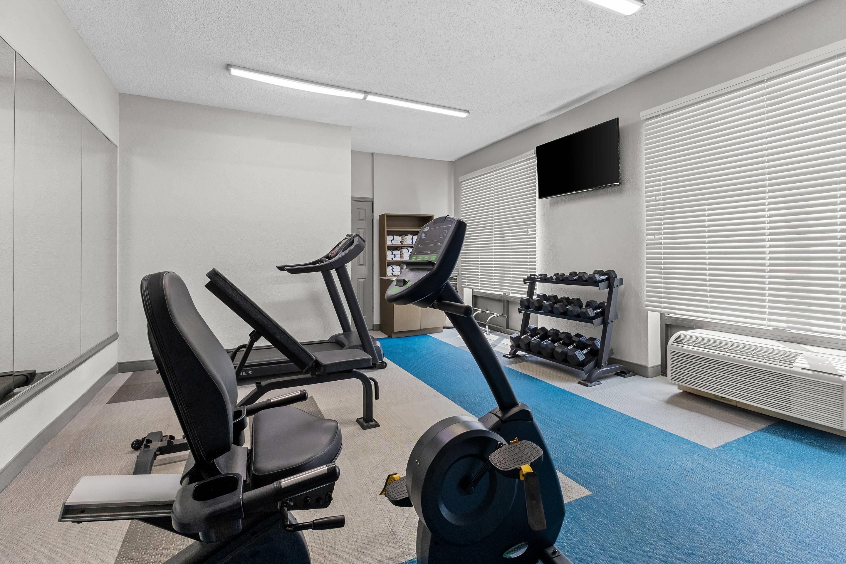 A gym with exercise equipment, a television, and a window with blinds.