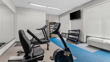 A gym with exercise equipment, a television, and a window with blinds.